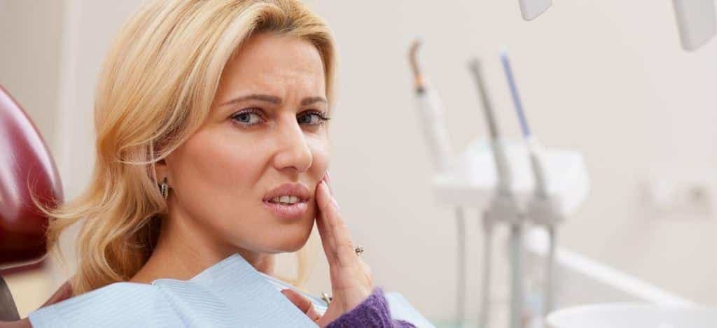 A patient holding a hand against their cheek in a dental chair