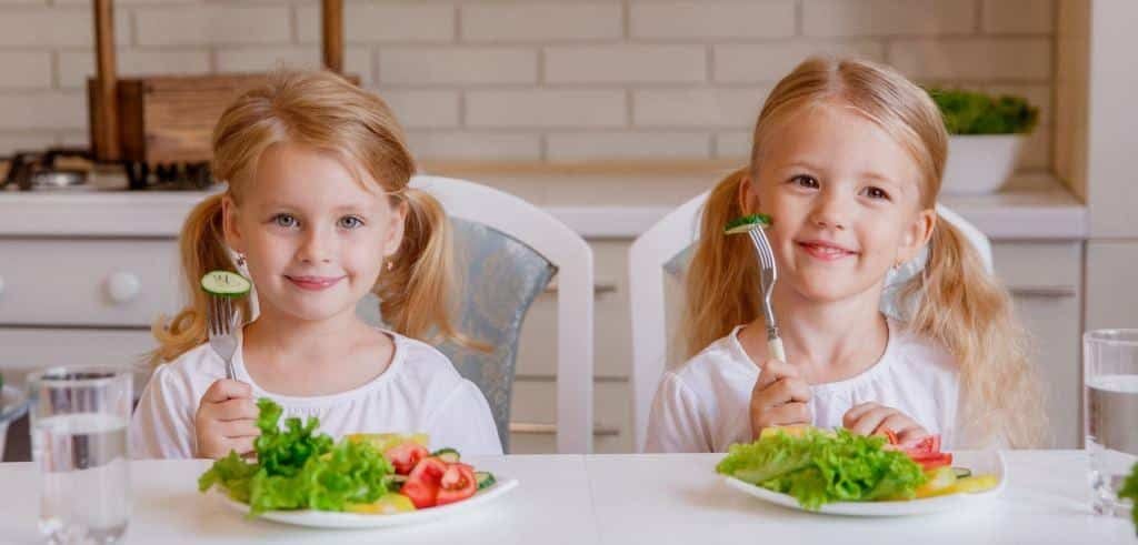 Two children sitting at a table with plates of salad