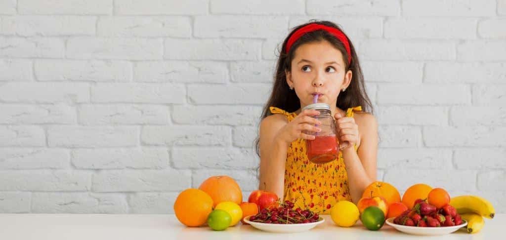 A child holding a drink at a table with fruit