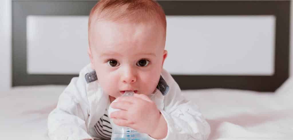 A baby lying on a bed with a hand near their mouth