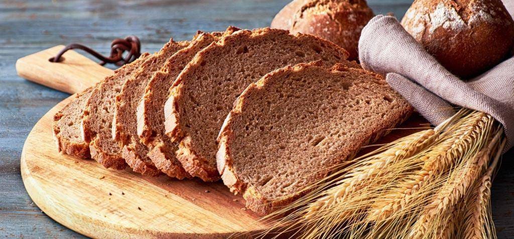 Sliced brown bread on a wooden board beside ears of grain