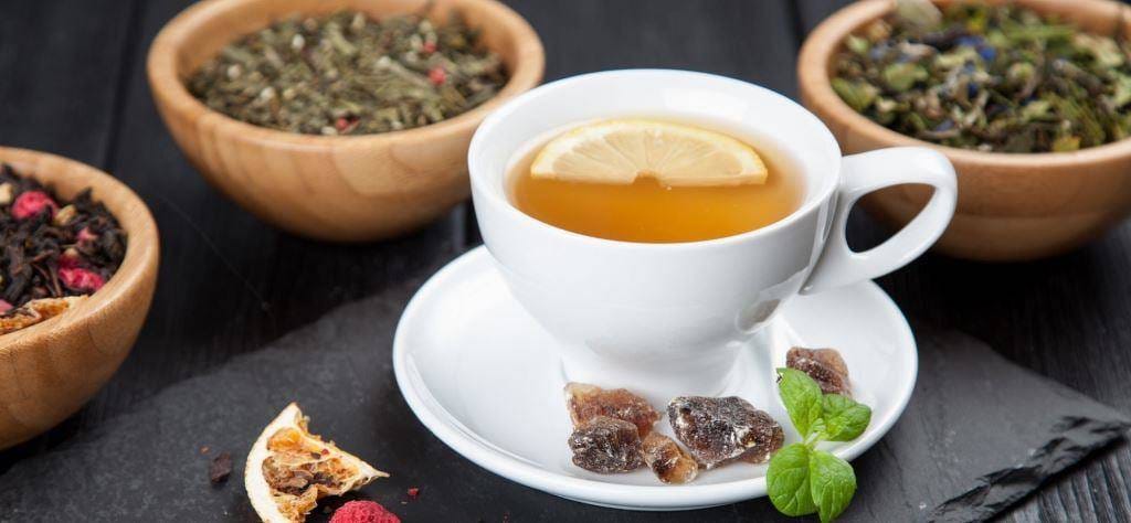 A cup of tea with lemon beside bowls of dried tea ingredients