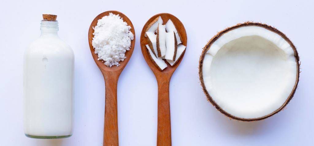 A halved coconut, coconut pieces and a bottle on a pale background