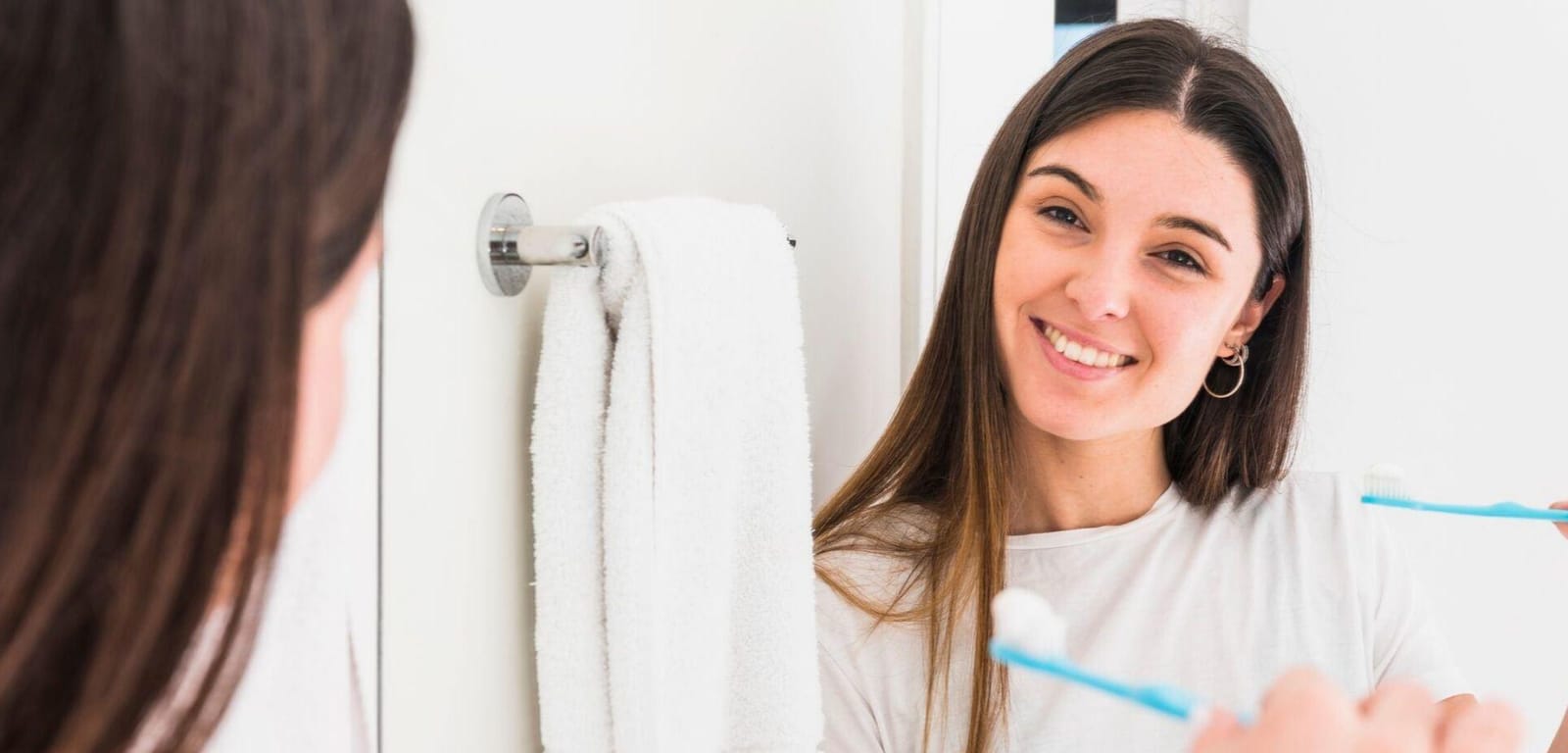 A woman holding a toothbrush while looking in a bathroom mirror