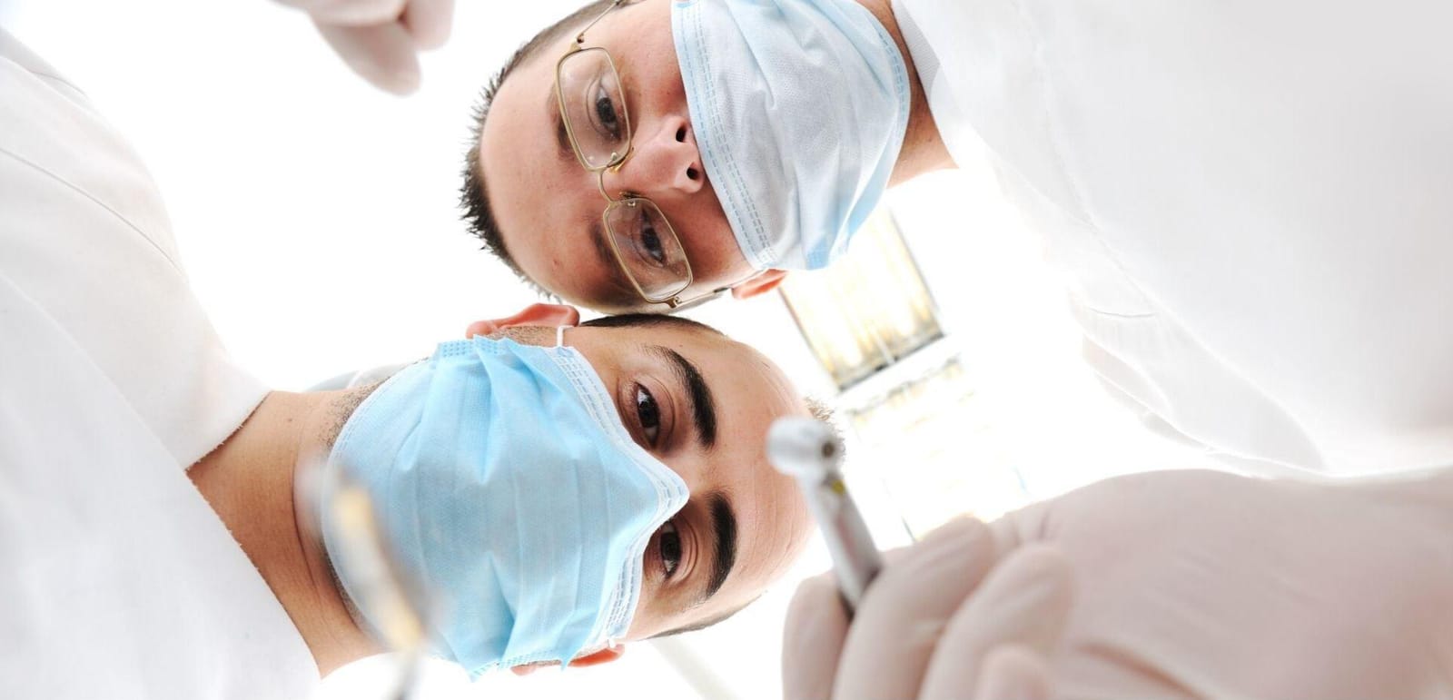 Two masked members of a dental team viewed from a patient’s position