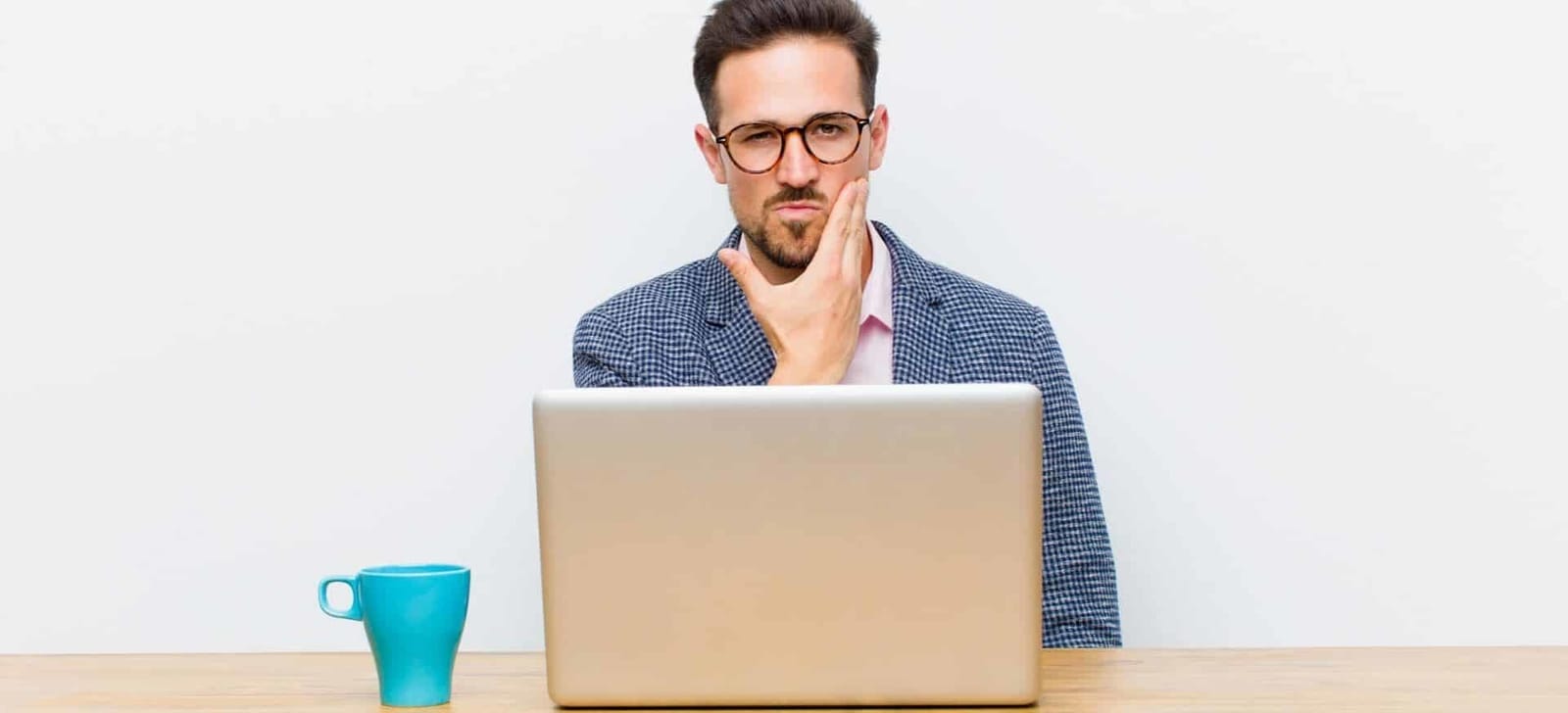 A man touching his cheek while sitting at a laptop