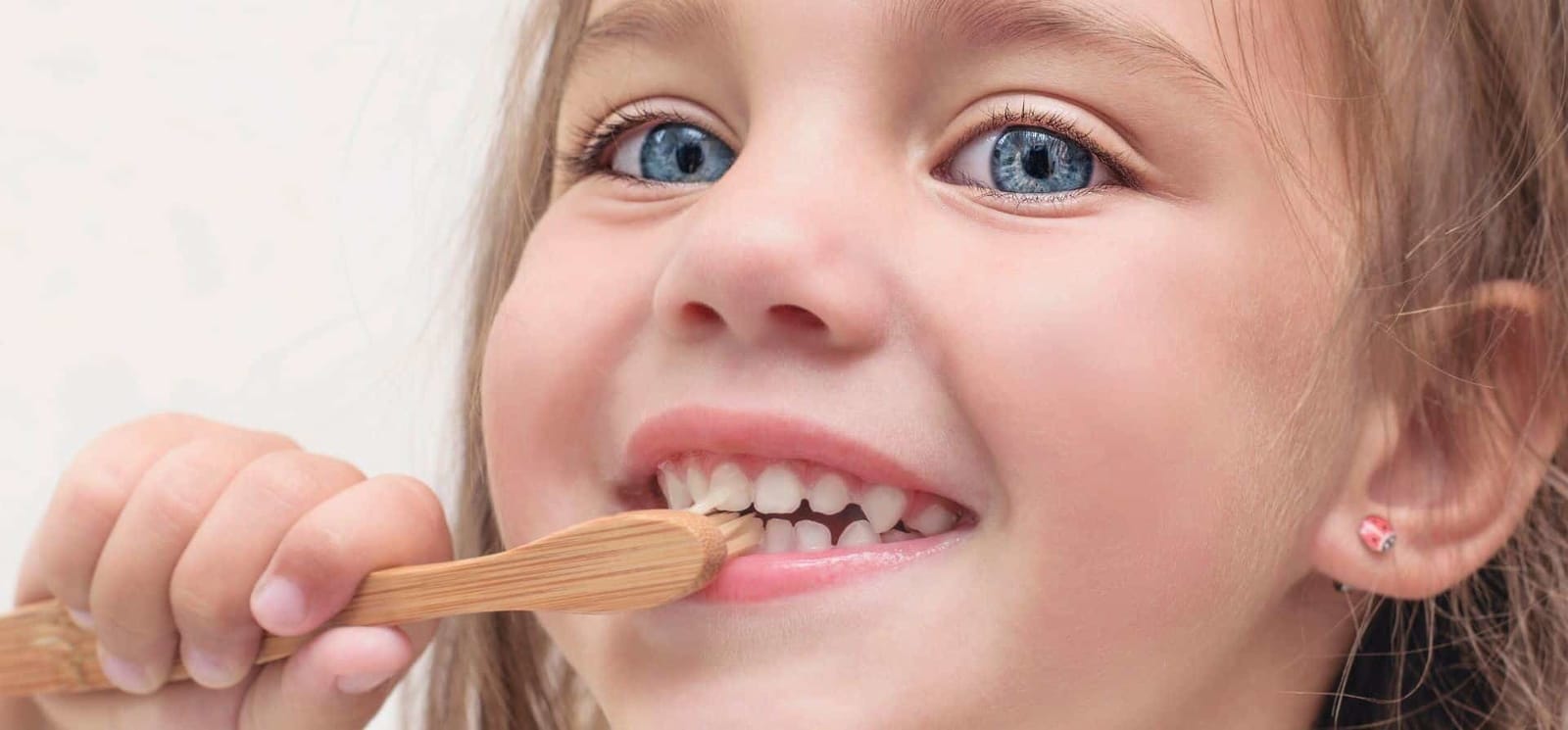 A child with a wooden toothbrush against their front teeth.