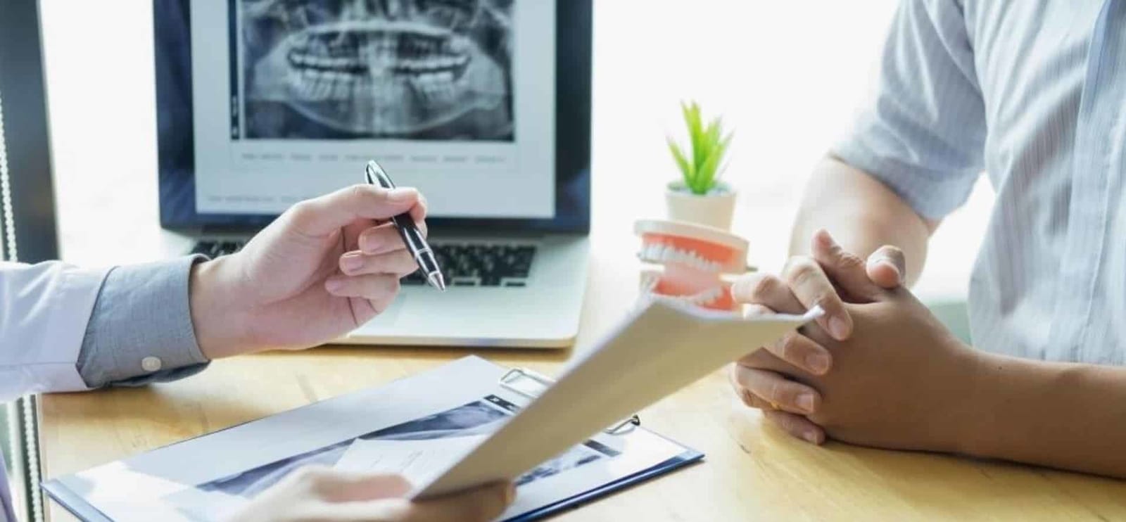 Dentist discussing information on a clipboard beside a laptop