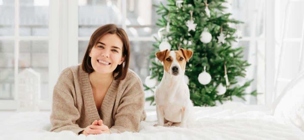 A woman and a dog beside a decorated Christmas tree