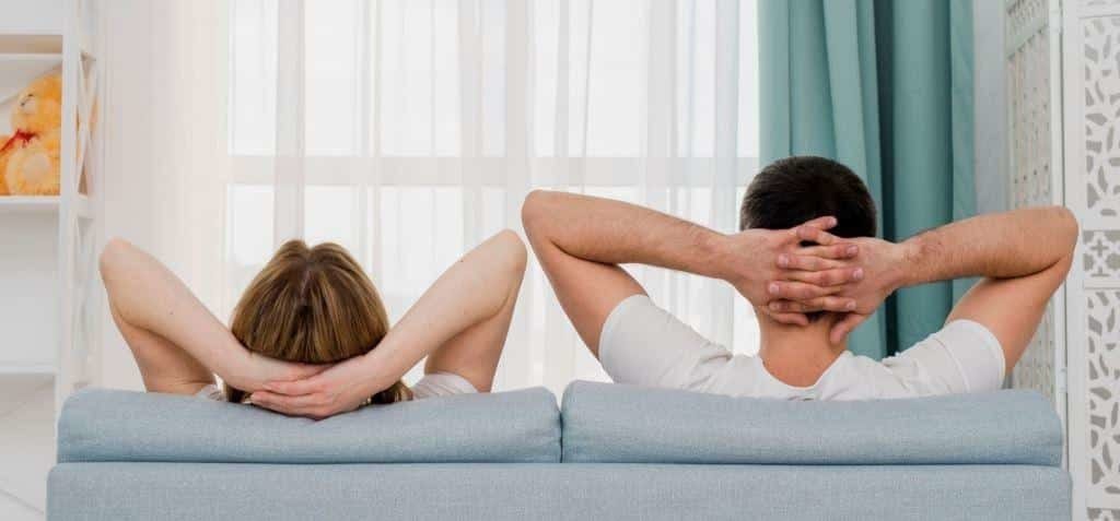 Two people sitting on a sofa with their hands behind their heads