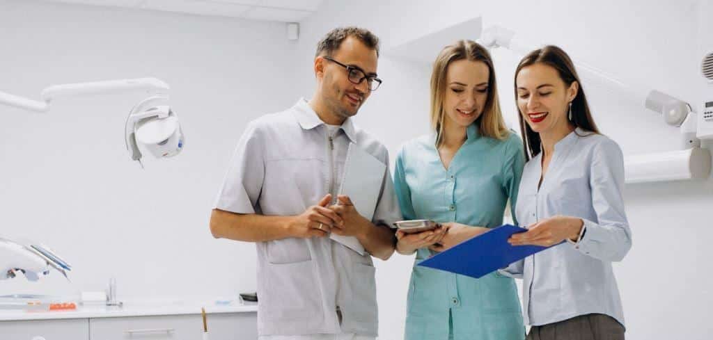 Three dental team members looking at a tablet and clipboard