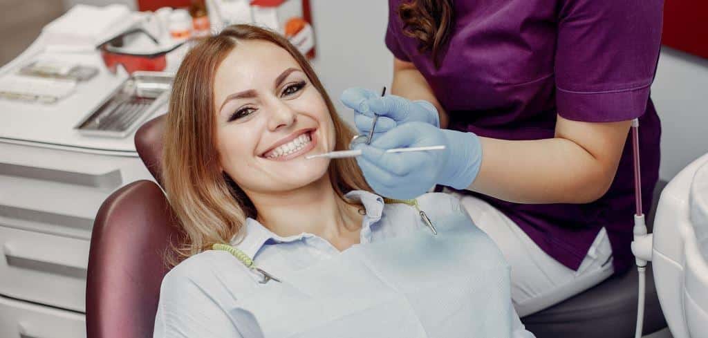 A patient in a dental chair beside gloved hands holding instruments