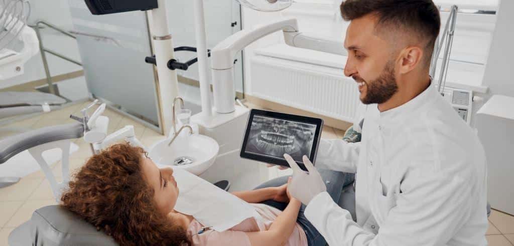 A clinician showing a dental X-ray on a tablet to a patient