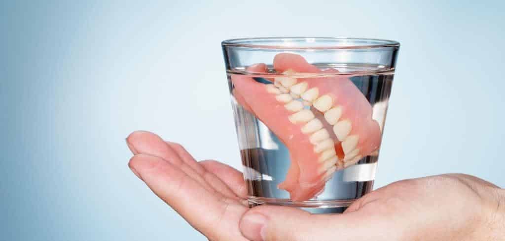 A denture in a glass of water held in a hand
