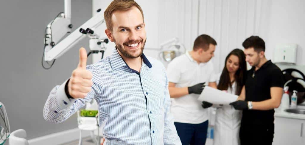 A smiling man giving a thumbs-up in a clinical setting