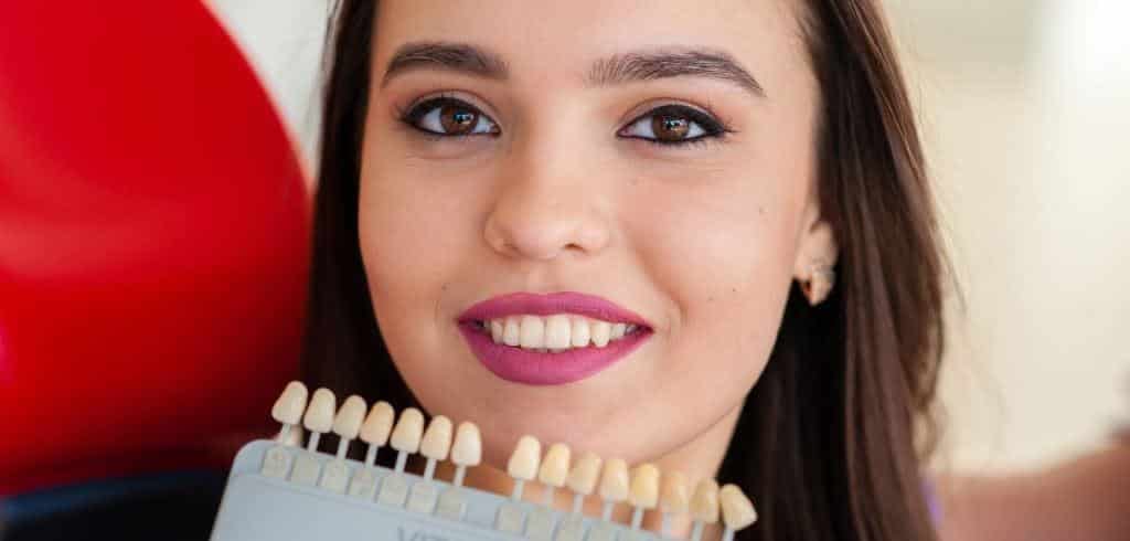 A smiling woman holding a tooth shade guide