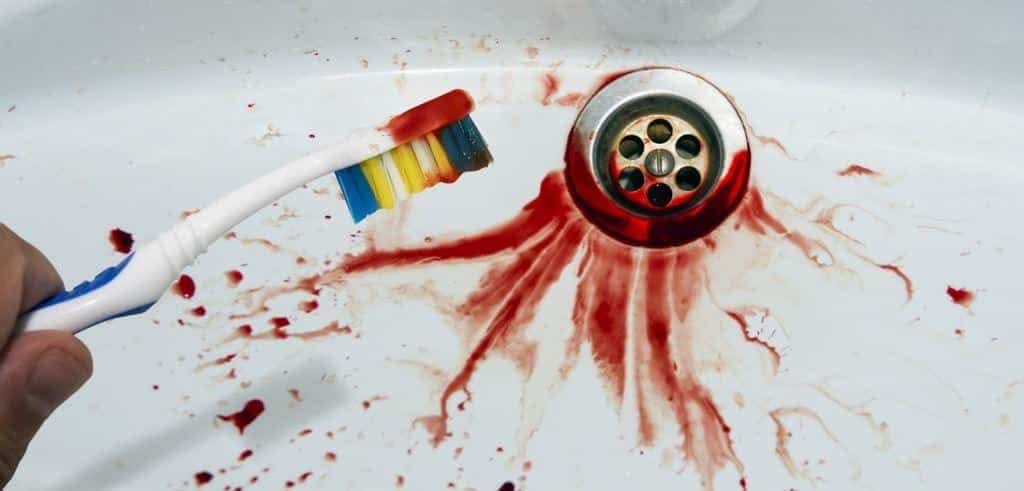 Toothbrush held over a basin with red staining around the drain
