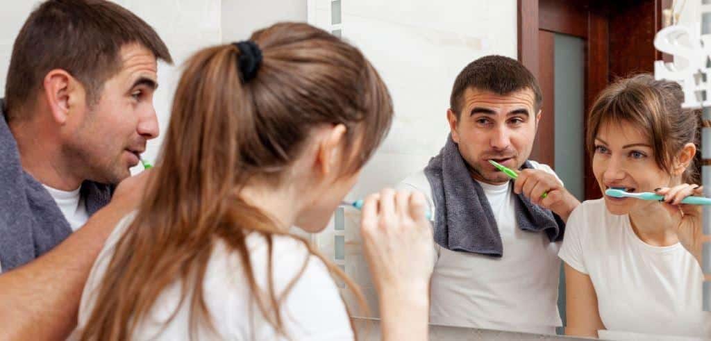 People brushing their teeth in front of a mirror