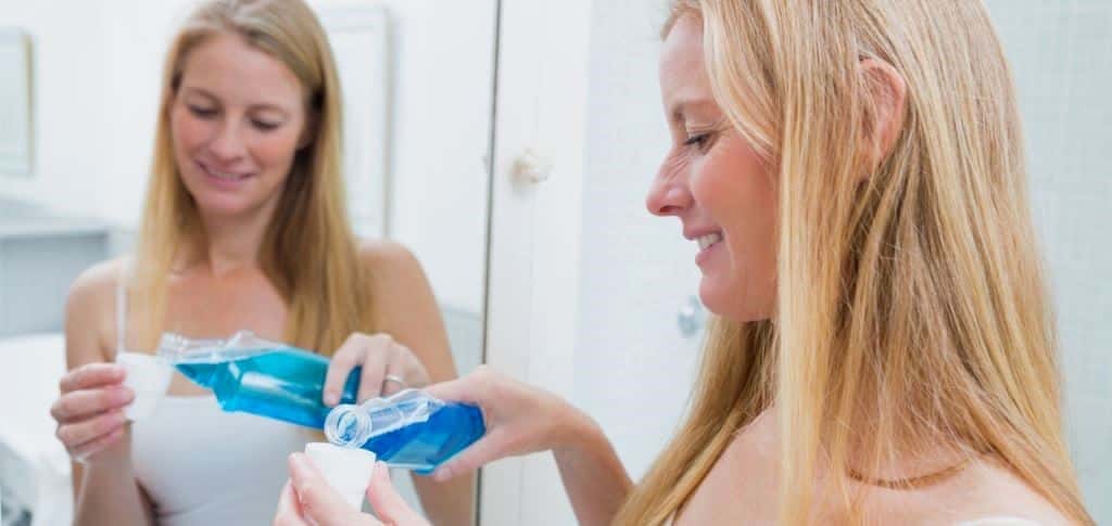 A woman pouring mouthwash into a cap beside a mirror