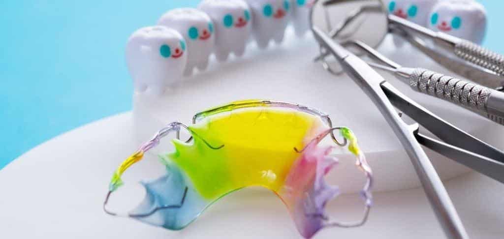 A colourful removable brace beside a dental model and instruments