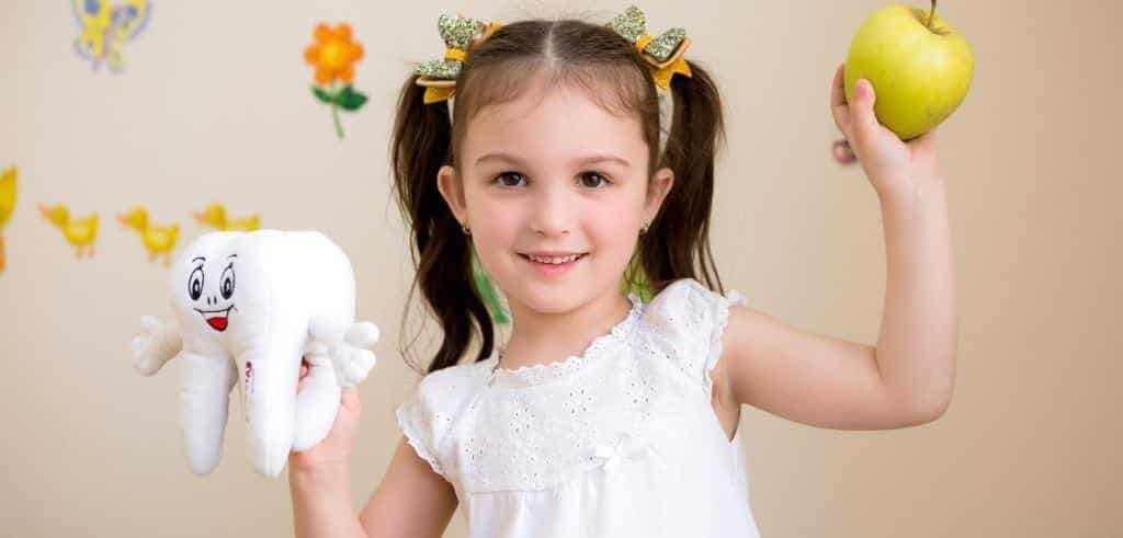 A child holding an apple and a tooth-shaped toy