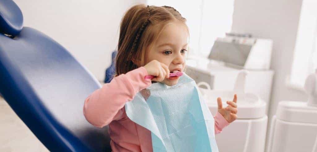 A child brushing their teeth while seated in a dental chair