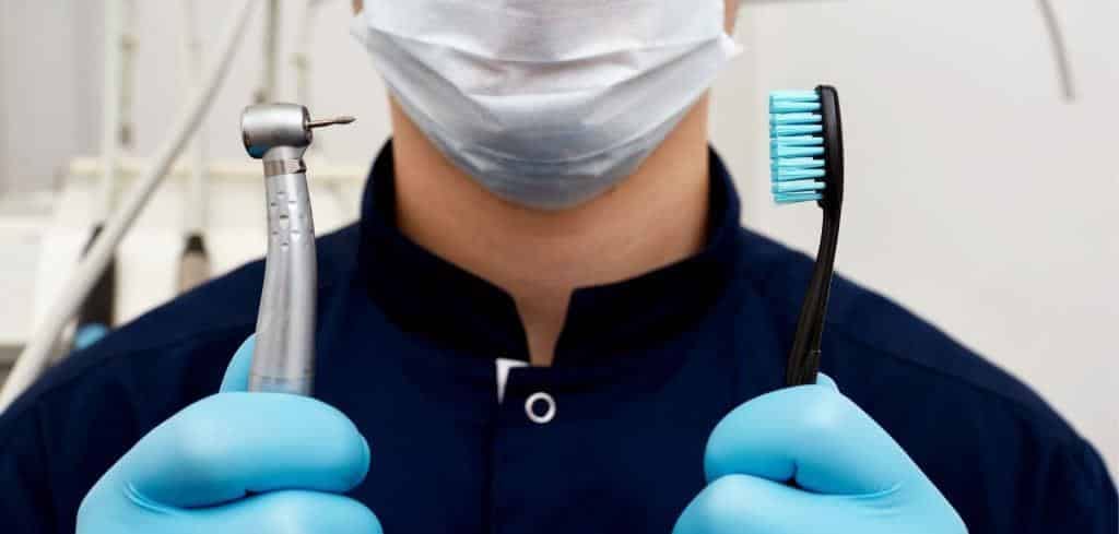 A clinician holding a toothbrush and a dental handpiece