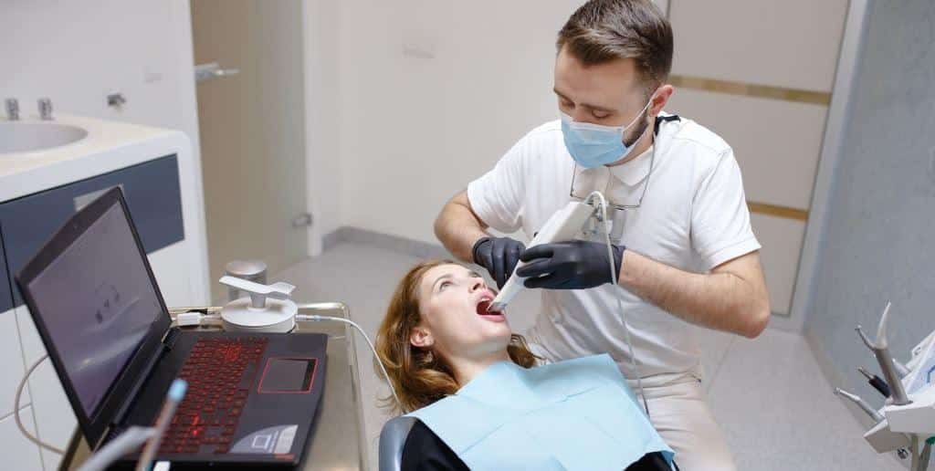 A dentist treating a patient beside a laptop