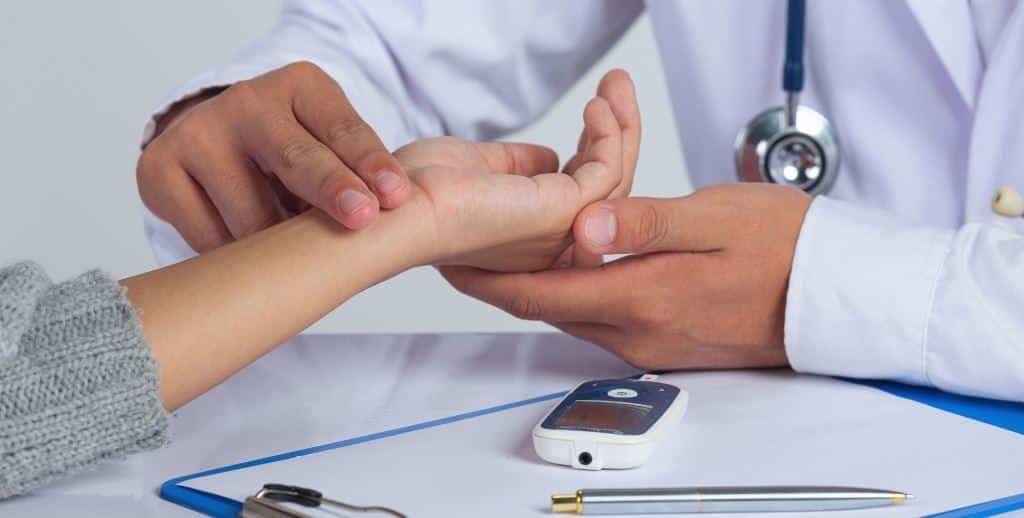 Clinician examining a patient’s hand beside a blood glucose meter