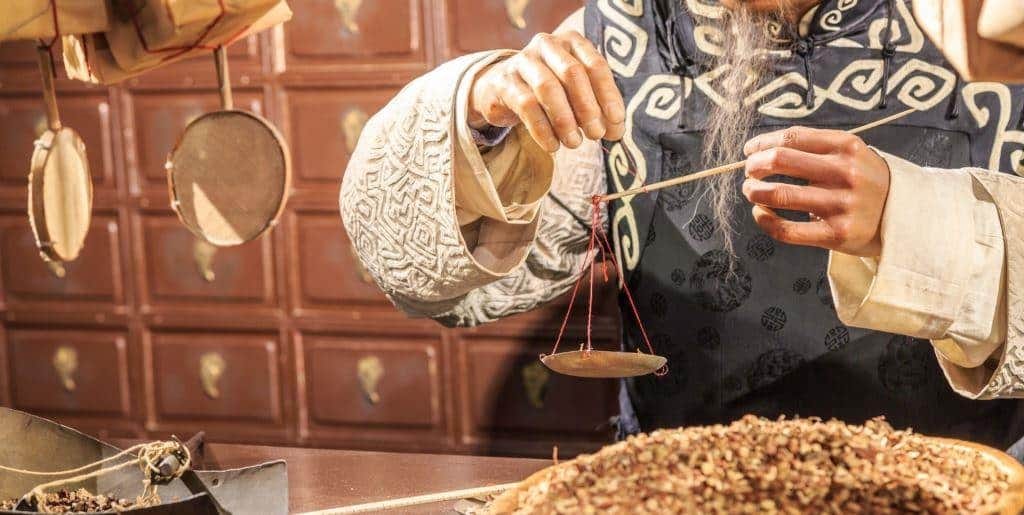 A person weighing ingredients on a balance in a traditional Chinese medicine setting