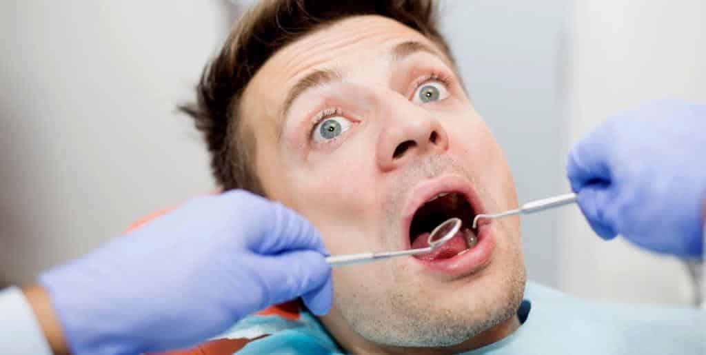 A patient with his mouth open while a dentist holds a mirror