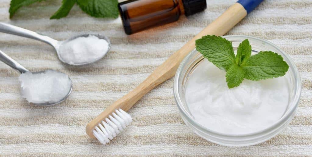 Bowls of white powder and oil beside a wooden toothbrush and mint