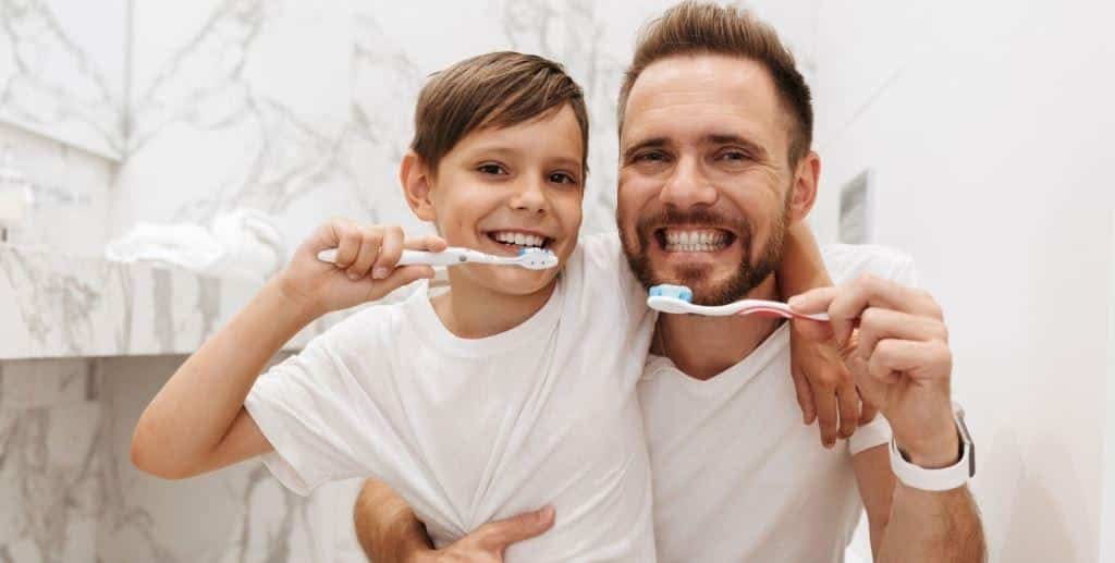 An adult and a child brushing their teeth together.