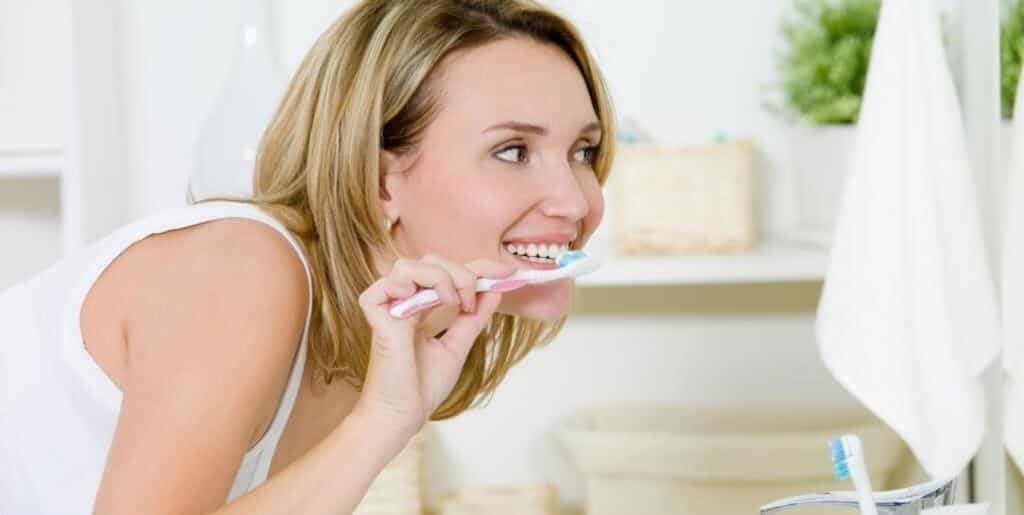 A woman brushing her teeth at a bathroom mirror