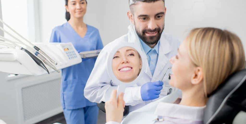 A patient holding a mirror while speaking with a dental team