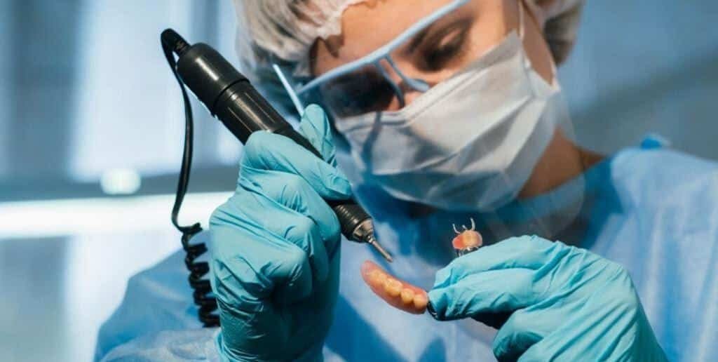 A person using a handpiece to work on a denture