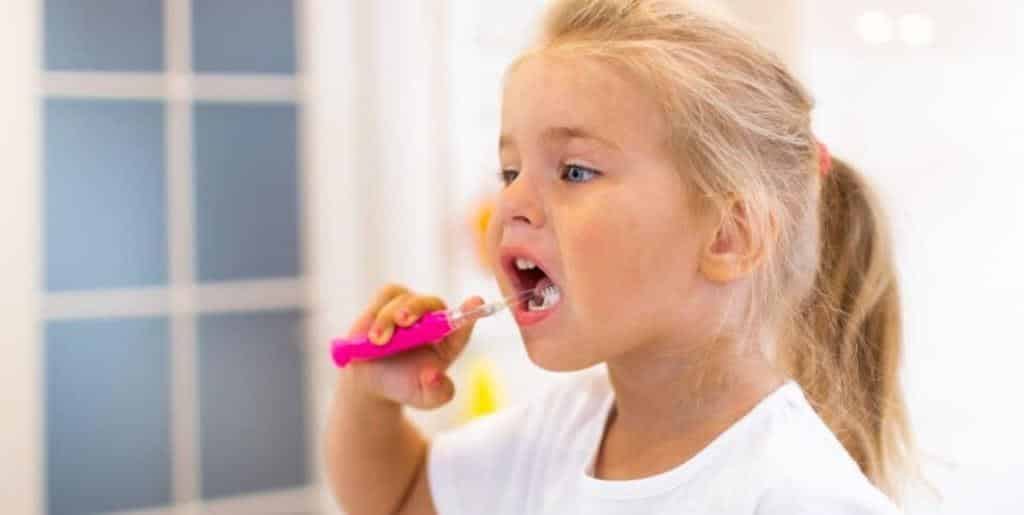 A child brushing their teeth with a pink toothbrush