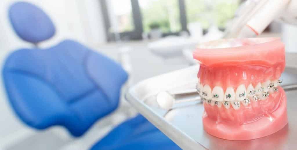 A model wearing fixed braces beside a dental chair