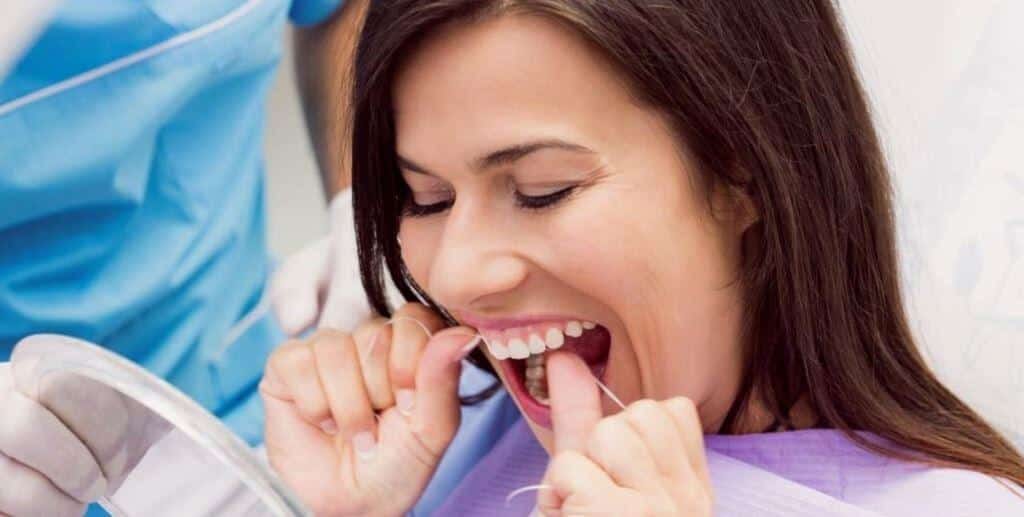 A person using dental floss while looking in a mirror