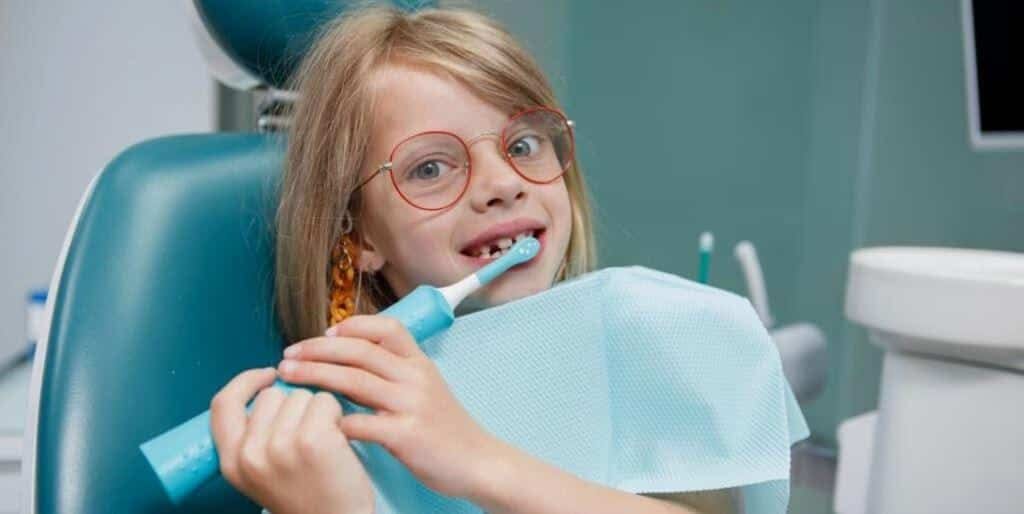 A child holding an electric toothbrush in a dental chair