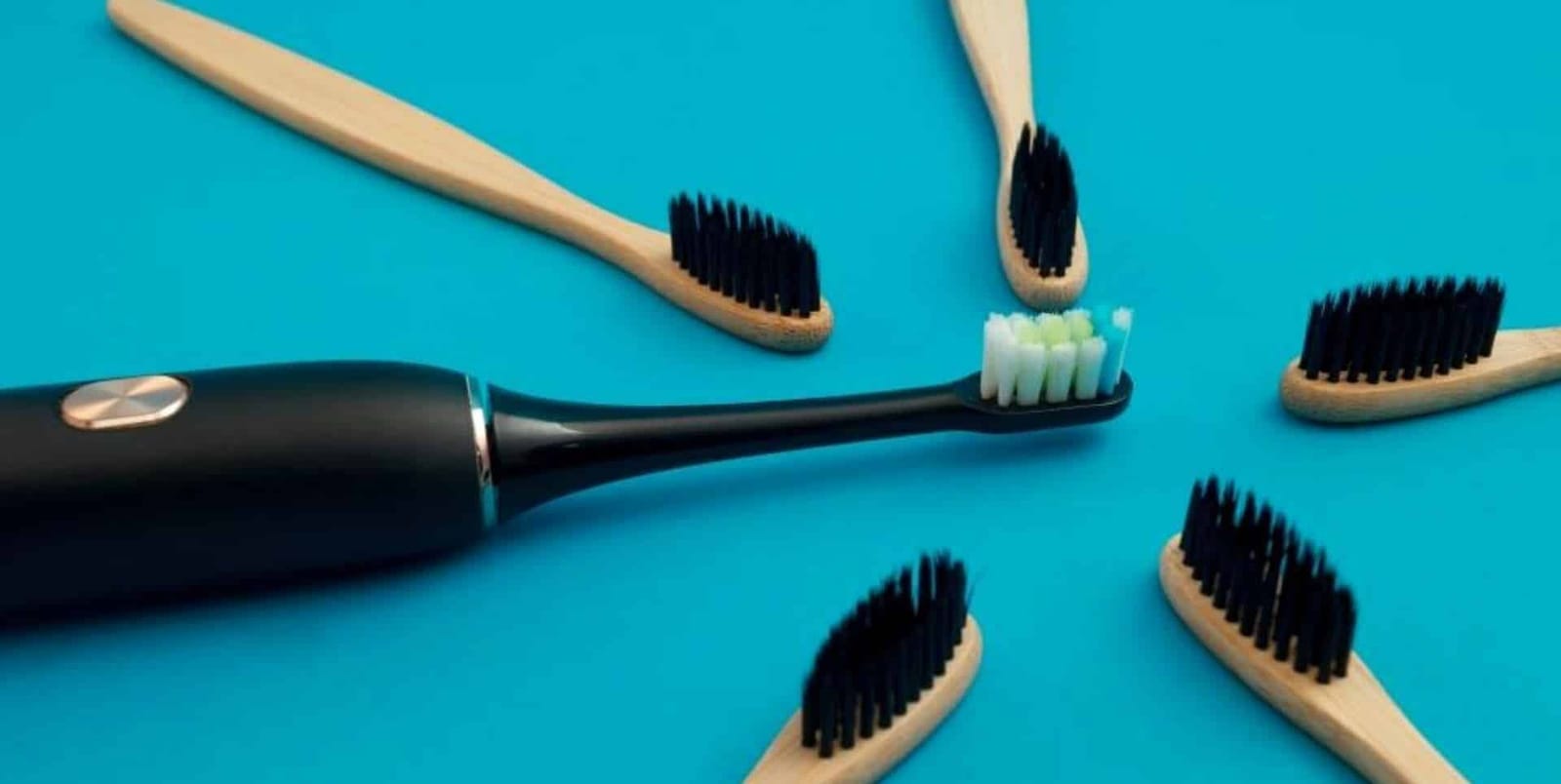 An electric toothbrush and wooden-handled toothbrushes on a blue background