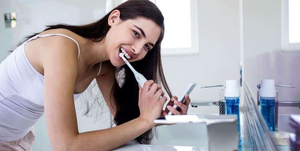 A woman brushing with an electric toothbrush beside a basin