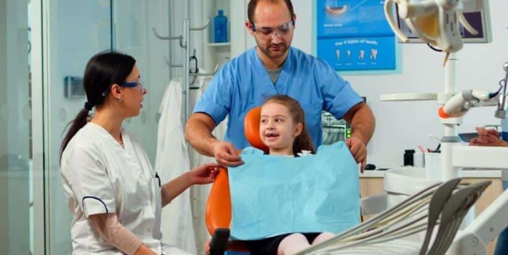 A girl in a dental chair with two members of the dental team