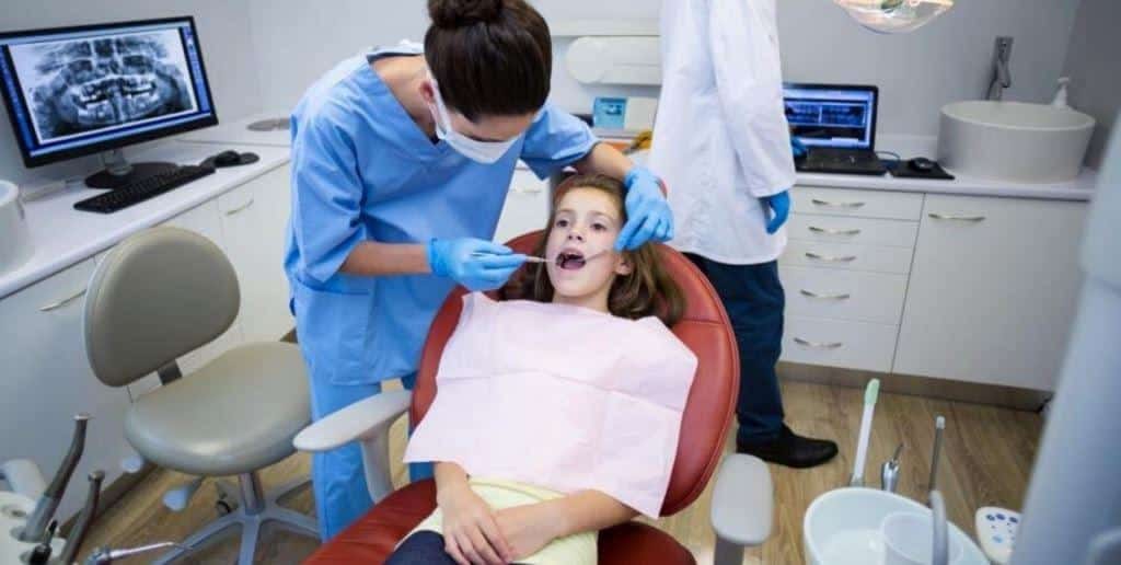 A clinician examining a girl’s mouth in a dental chair