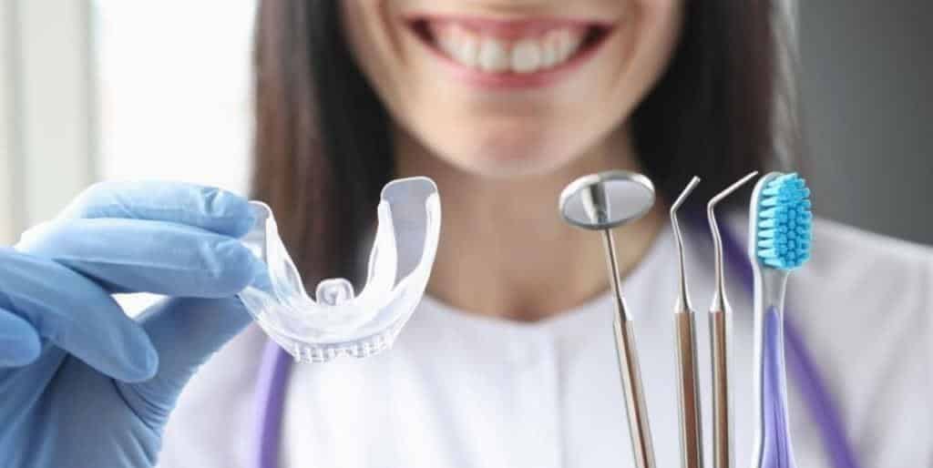 A person holding a clear dental appliance beside dental instruments