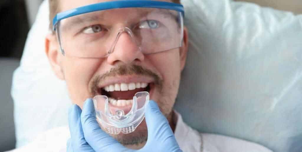 A gloved hand holding a clear dental appliance near a patient’s mouth