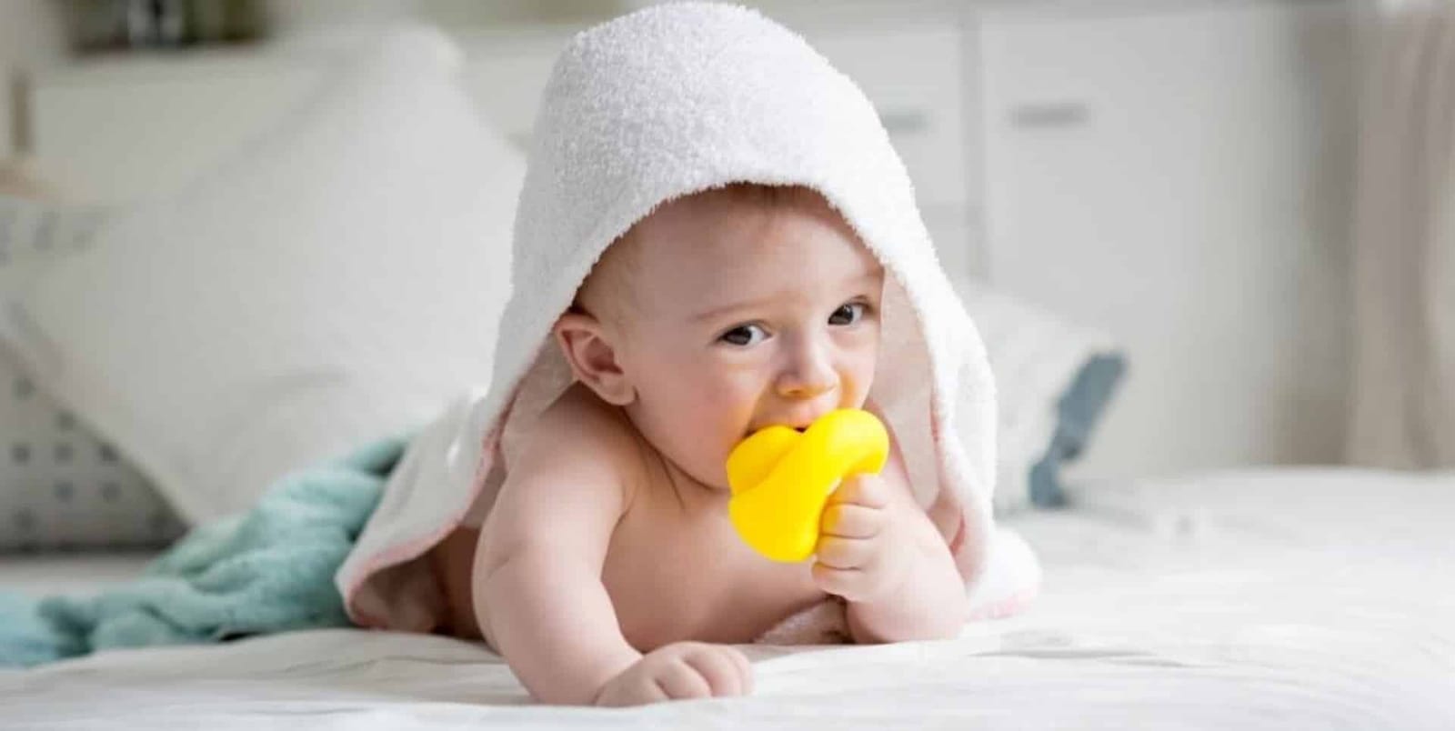 A baby with a towel over their head holding a yellow teether