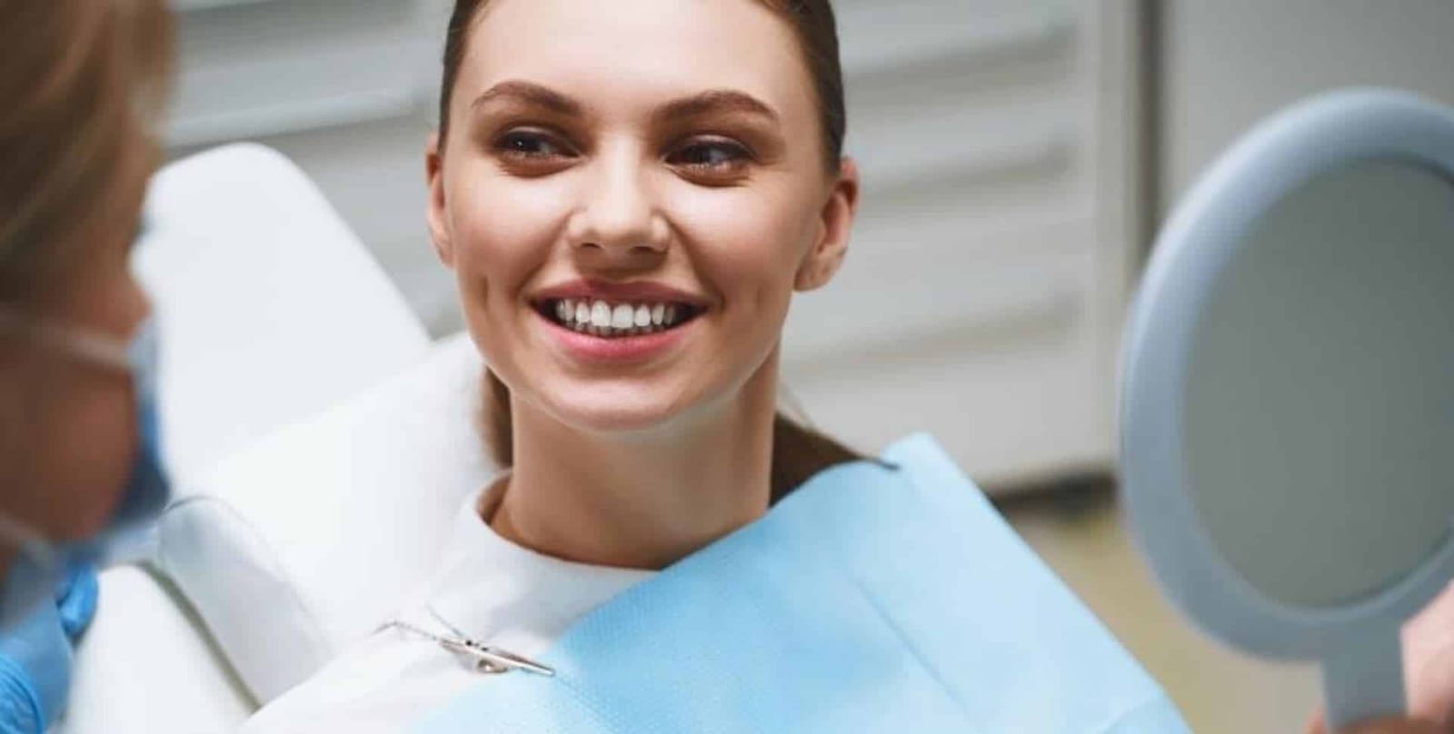 A patient smiling while holding a mirror in a dental chair.