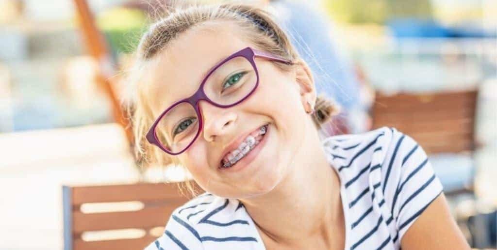 A smiling child wearing glasses and fixed braces