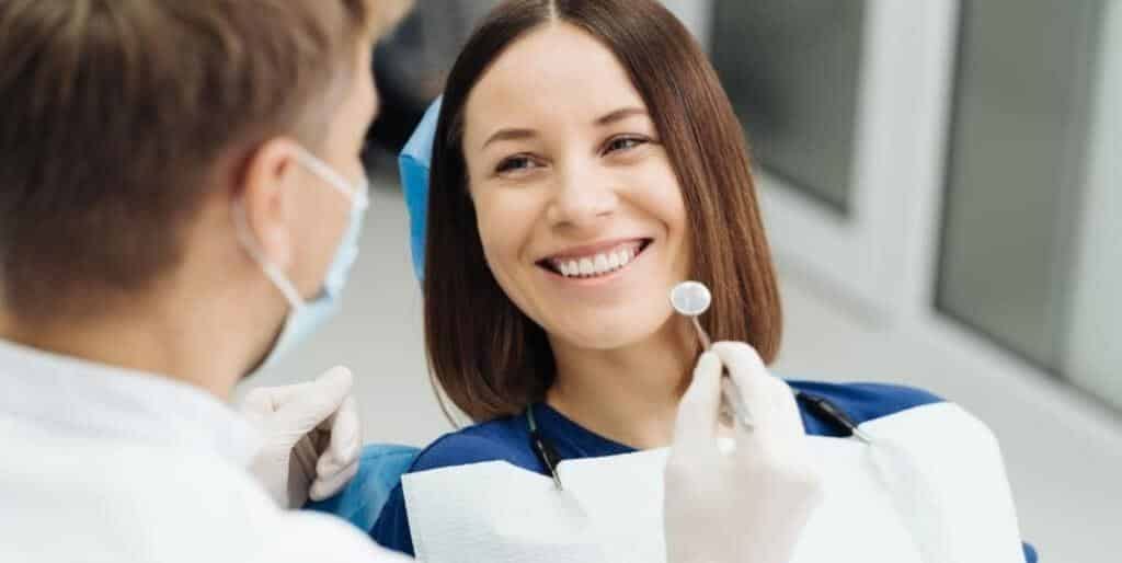 A patient looking at her teeth in a mirror beside a clinician